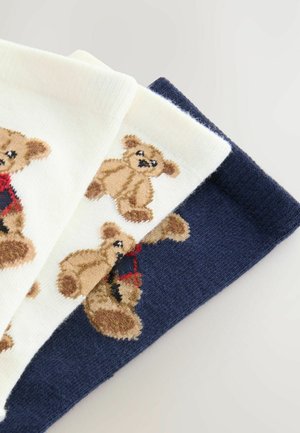Drei Paar Socken: ein cremefarbiges Paar mit Bärendesign, ein marineblaues Paar mit Bär sowie ein strukturiertes Strickpaar in Dunkelblau. Jedes Paar hat Plüschbärenakzenten.