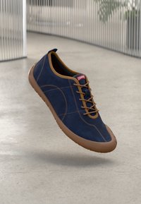 Baskets en daim bleu marine avec des accents marron, présentant un bout arrondi, des lacets fins et une semelle en caoutchouc. Étiquette de la marque sur la languette.