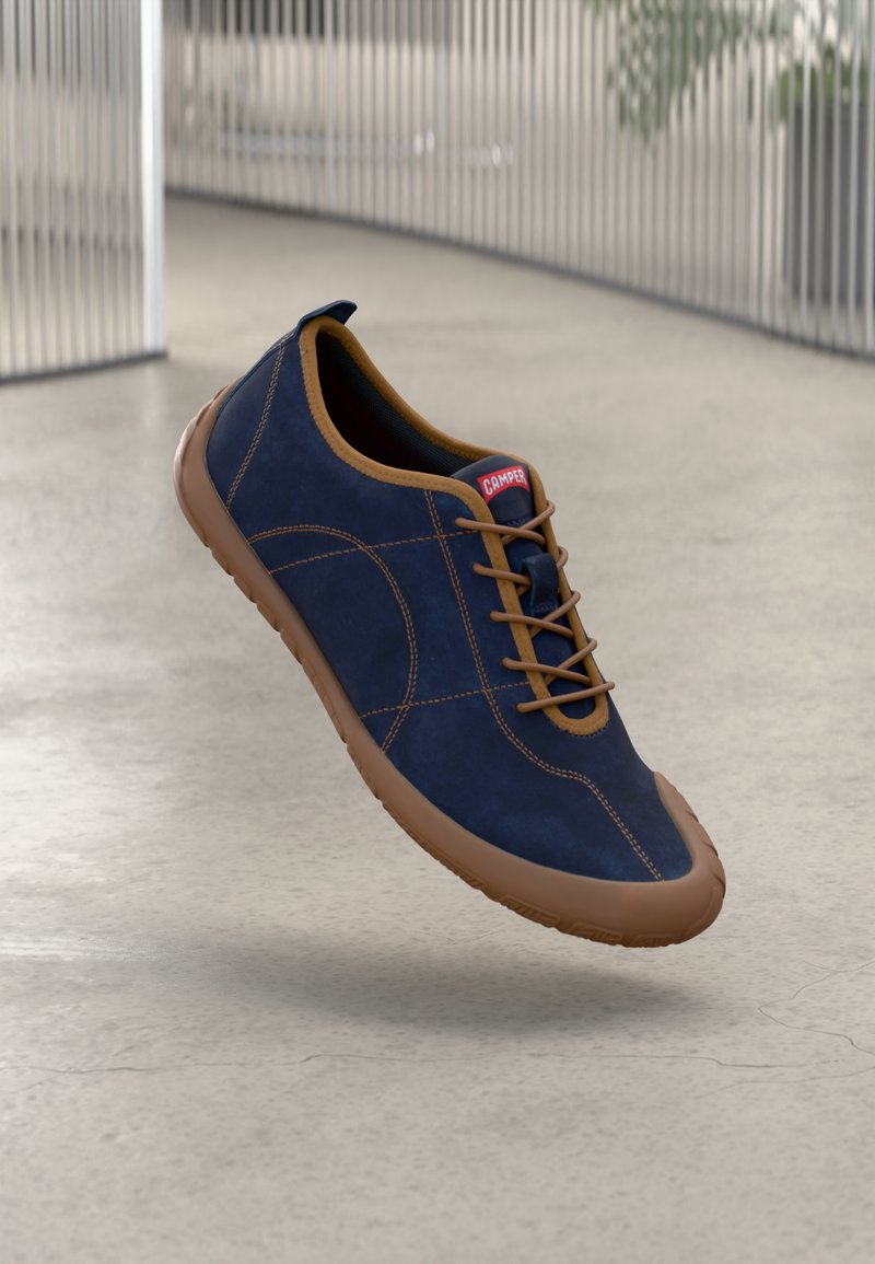 Baskets en daim bleu marine avec des accents marron, présentant un bout arrondi, des lacets fins et une semelle en caoutchouc. Étiquette de la marque sur la languette.