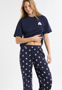 Granatowy bawełniany t-shirt z grafiką białego pudla; zestawiony z granatowymi spodniami z wzorem pudla i drobnymi złotymi kropkami na całej powierzchni.