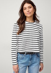 Zwart-wit gestreept lange mouwen top met een ronde hals, gemaakt van zacht materiaal, gecombineerd met hoog getailleerde lichtblauwe jeans en een zwarte riem.