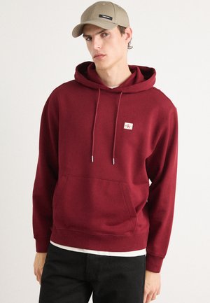 Bordeaux hoodie met een voortasje, koordjes en een klein logo-opdruk. Zacht materiaal en ribgebreide manchetten aan de onderkant.