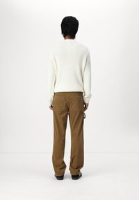 Sweter z teksturowanej kremowej dzianiny z długimi rękawami, w połączeniu z luźnymi brązowymi spodniami z korduroju z dwoma tylnymi kieszeniami i bocznymi pętelkami.