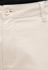 Μπεζ βαμβακερό παντελόνι με λεία υφή, εμπρόσθιο κουμπί και ορατές ραφές κατά μήκος των ενώσεων.