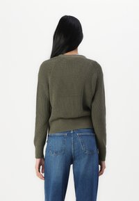 Olivovo zelený pletený sveter s ribbovanou textúrou, raglánovými rukávmi a mierne skrátenou dĺžkou, kombinovaný s modrými džínsy s vysokým pásom.