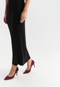 Czarna midi sukienka z falbaniastym dołem i dopasowaną sylwetką, w połączeniu z burgundowymi zamszowymi szpilkami z wysmukłą szpilką.