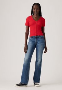Red fitted ribbed button-up shirt, blue flared jeans, and black sneakers with white soles. The outfit is casual and contemporary.