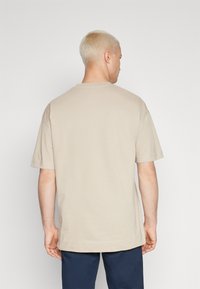 Lys beige kortermet T-skjorte med rund hals og rett søm, laget av myk bomullsstoff. Enkel design uten synlige trykk eller mønstre.