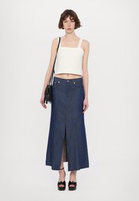 Denim maxi-seelik kõrge lõhiku ja nurkselgestega, koos tekstuuriga valge lühikese topsiga. Aksessuaarid sisaldavad musta frantsi kotti ja platvormkingi.