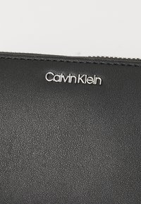 Czarny skórzany portfel o fakturze, z srebrnym logo "Calvin Klein". Posiada zamek błyskawiczny oraz gładkie detale szwów.
