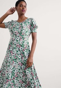 Floral print dress with puff sleeves; green background with white, pink, and blue flowers; knee-length and flowing design.