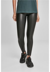 Leggings noirs brillants en matériau extensible, design ajusté, associés à des baskets de sport noires et à un t-shirt vert foncé.