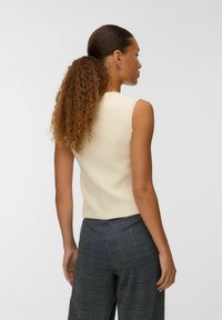 Top sans manches crème avec une texture lisse et une coupe ajustée, associé à un pantalon à carreaux gris à jambes larges et à la coupe sur mesure.