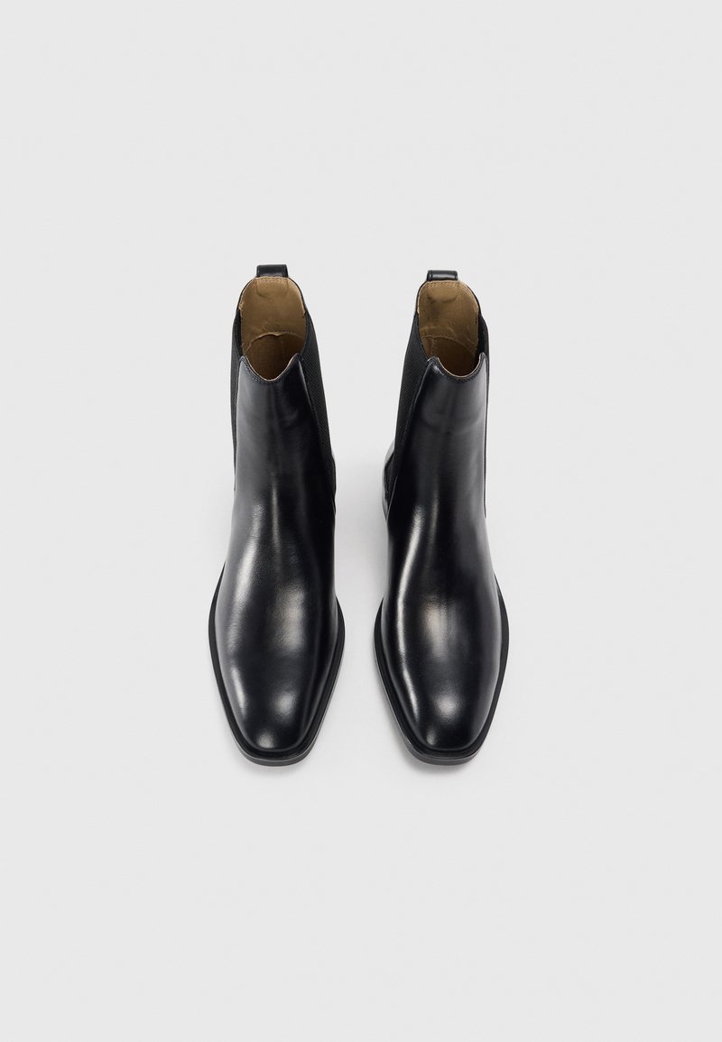 Bottes noires en cuir, à la finition lisse et au design à bout pointu. Elles sont dotées d'un panneau latéral élastique court pour un enfilage facile.