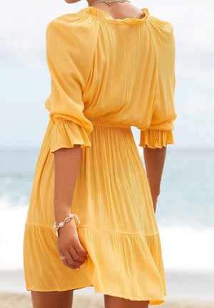 Robe jaune fluide en tissu léger, avec un col à volants, des manches trois-quarts et une taille froncée avec un ourlet à paliers.