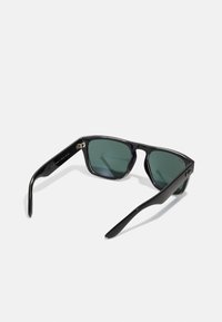 Ochelari de soare din plastic negru cu lentile verzi. Ramă de formă pătrată, textură netedă, balamale vizibile pe temple. Fără modele sau accente vizibile.