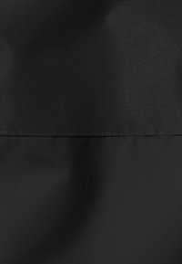 Tessuto nero con una texture liscia e opaca, caratterizzato da un design bicolore con una cucitura orizzontale ben definita che divide le sezioni superiore e inferiore.