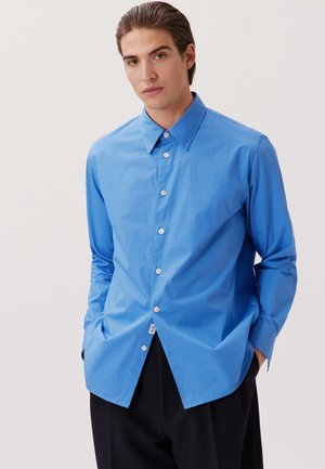Camicia azzurro chiaro con colletto classico, maniche lunghe e orlo curvo. Realizzata in tessuto morbido con bottoni bianchi e un discreto dettaglio dell'etichetta.