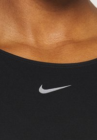 Gros plan sur la partie supérieure de la poitrine vêtue d'un vêtement de sport noir avec le logo Nike swoosh blanc centré sous la clavicule.