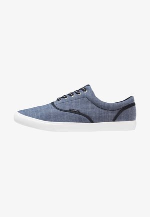 Baskets basses bleues avec semelle blanche, bordure noire, lacets noirs et étiquette "Jack & Jones" sur le côté.