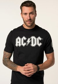 Zwart T-shirt met korte mouwen met een opvallend wit AC/DC-logo. Van katoen met een soepele textuur. Tatoeage zichtbaar op de linkermouw.