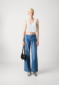 White cropped vest top with vertical stripes and front buttons, paired with high-waisted blue wide-leg denim jeans and silver shoes.