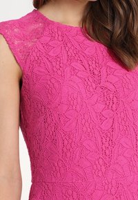 Knappt rosa spetsklänning med ett blommönster, korta ärmar och en åtsittande bodice. Texturerad tyg ger ett lager-på-lager utseende.