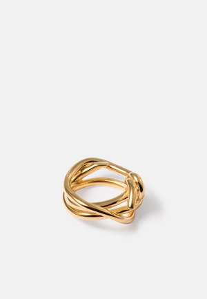 Goudkleurige metalen ring met in elkaar verweven, gladde, ronde bandjes die een modern, sculpturaal ontwerp vormen op een witte achtergrond.