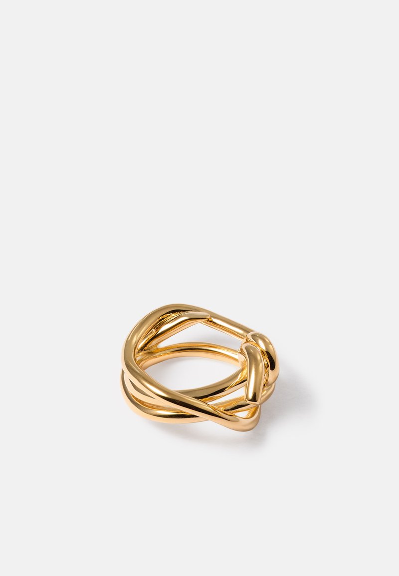 Guldtonet metalring med sammenflettede, glatte, afrundede bånd, der danner et moderne, skulpturelt design på en hvid baggrund.