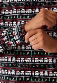 Musta napillinen paita, jossa on juhlateemainen kuvio stormtroopereista, karkkikepeistä, joulukuusista ja sukista punaisena ja vihreänä.