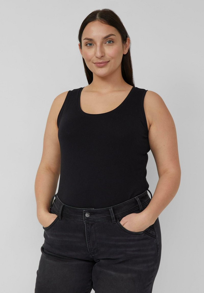 Schwarzes Trägertop aus Baumwolle mit runder Ausschnitt und breiten Trägern, kombiniert mit dunkler Jeans. Der Stoff ist glatt und eng anliegend.