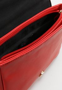 Borsa a mano in pelle rossa dalla texture liscia, con chiusura superiore a zip e interno in tessuto nero. Sono visibili dettagli in metallo dorato.