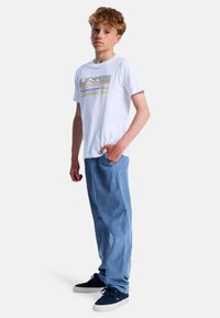 T-shirt blanc à manches courtes avec un graphique coloré de montagnes, associé à un pantalon en denim droit bleu clair, et des baskets navy.