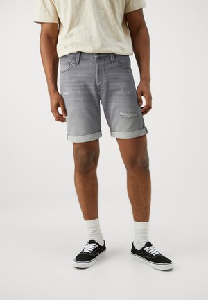 Graue Denim-Shorts mit verwaschenen Akzenten, umgeschlagenen Säumen und Fünf-Taschen-Design, kombiniert mit schwarzen Sneakern und weißen Crew-Socken.