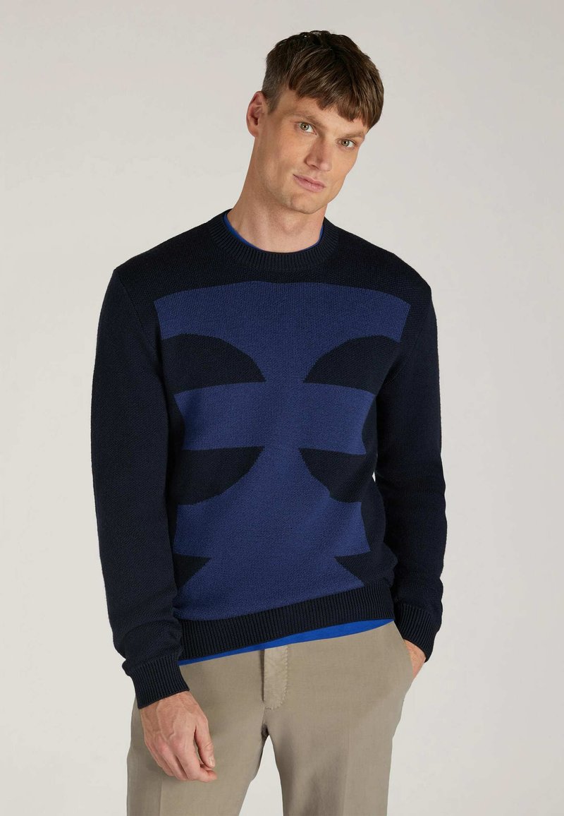 Navy blue crew-neck sweater featuring geometric designs in varying shades of blue, knit texture, and ribbed cuffs and hem.