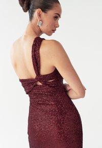 Burgundia tikitud õhtukleit keeruka seljaga ja avatud lõigetega, millel on vormiv siluett ja sile tekstuur.