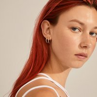 Boucles d'oreilles en forme de créoles couleur or présentées sur un modèle aux cheveux roux, arborant un design texturé et deux créoles distinctes empilées ensemble.