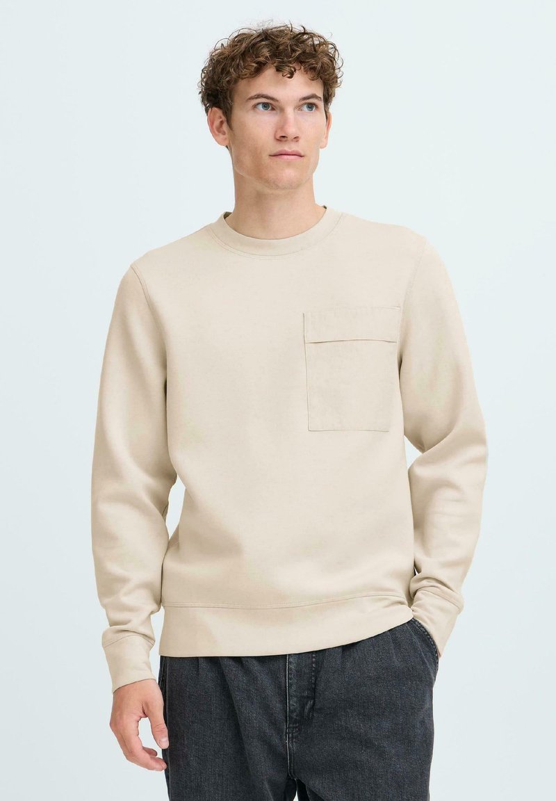 Beige sweatshirt met lange mouwen, ronde hals en een voorzak. Zachte textuur, eenvoudig ontwerp en een relaxte pasvorm.