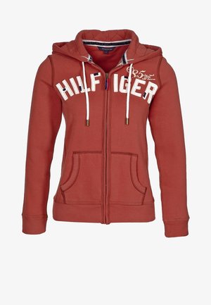 Sweat à capuche zippé couleur rouille avec cordons blancs, poches avant et texte "HILFIGER" sur la poitrine.