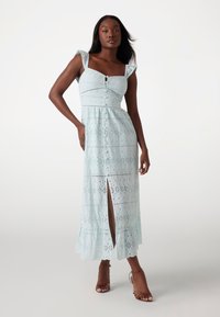 Light blue lace dress with square neckline, short ruffled sleeves, and front slit. Textured floral patterns throughout. Brown heeled sandals.