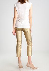 Pantalones cortos metálicos dorados, diseño ajustado, textura suave. Combinados con una blusa de manga corta color crema. Marca mínima en la parte posterior de la blusa.