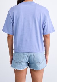 T-shirt a maniche corte di colore viola chiaro con vestibilità comoda, orlo rifinito e tessuto morbido, abbinata a shorts di jeans sfrangiati.