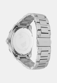 Srebrn ročni sat iz nerjavečega jekla z robustnim povezovalnim pasom. Na zadnji strani ohišja je vgraviran logotip blagovne znamke in podrobnosti o vodoodporni zasnovi.