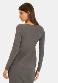 Szary prążkowany sweter z długimi rękawami, ozdobiony metalowymi detalami wzdłuż rękawów oraz okrągłym dekoltem.