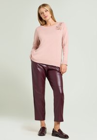 Maglione rosa chiaro lavorato a maglia con decorazioni floreali sulla spalla, abbinato a pantaloni in pelle bordeaux a vita alta e scarpe nere lucide.