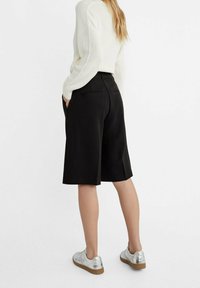 Shorts negros de corte a medida, hechos de una tela suave, con bolsillos laterales y un ajuste ligeramente holgado. Combinados con un suéter de punto color crema y zapatillas metálicas.