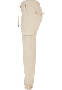 Pantalon cargo beige avec taille et chevilles élastiques, poches avant et une poche à rabat sur la cuisse.
