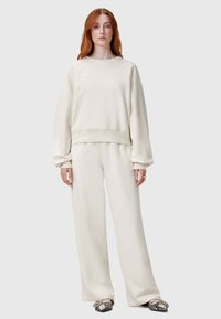 Cremfarbener Sweatshirt und weite Hose Set, das über einen Rundhalsausschnitt, gerippte Bündchen und eine weiche Textur verfügt. Akzentuiert mit gemustertem Schuhwerk.