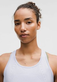 Top deportivo de color gris claro con textura perforada y escote redondo. Se ven los tirantes del sujetador en verde por debajo. Acabado de tela suave.