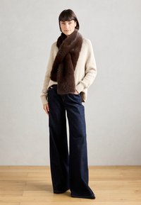 Brown fur scarf draped over a light beige knitted sweater, paired with dark blue wide-leg jeans. Smooth textures and neutral colors dominate.